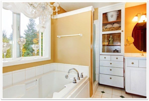 to the left is a window overseeing trees above a lovely bathtub and a shower and cabinets of to the right of it