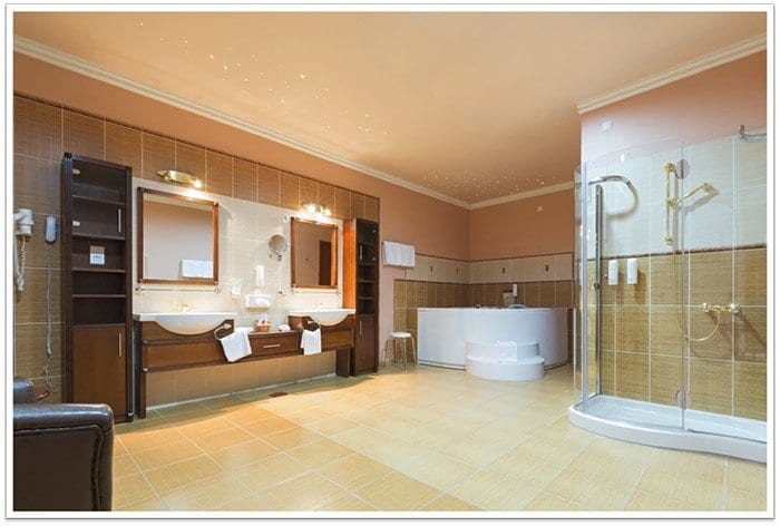 very large bathroom with a stnading shower to the right, a jacuzzi bathtub in the far middle of the room, and two sinks with two mirrors to the left.