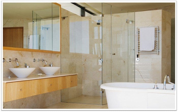 frameless glass shower in the back of pictures with a bathtub and two sinks in-front of it