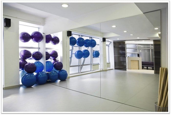 a gym with mirrors all along the wall and workout balls in a corner, both purple and blue balls