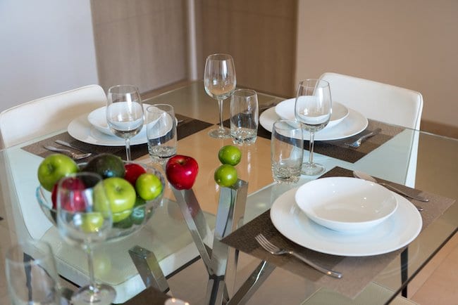 glass dining table with fruit and silverware placed neatly on top of the table