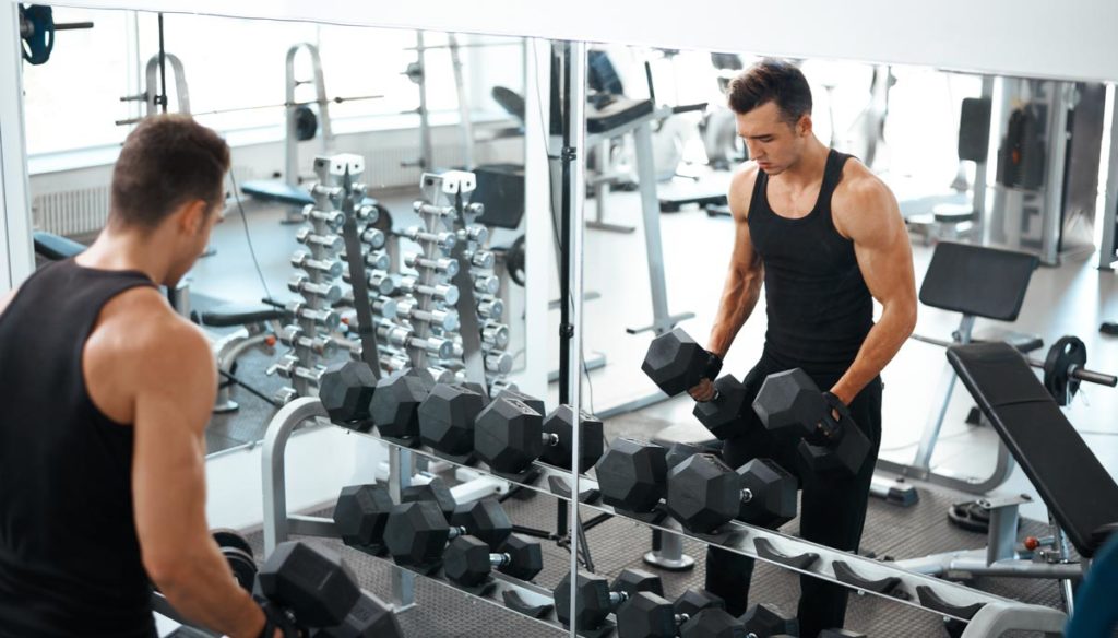 Man lifting weights in front of glass gym mirror wall.